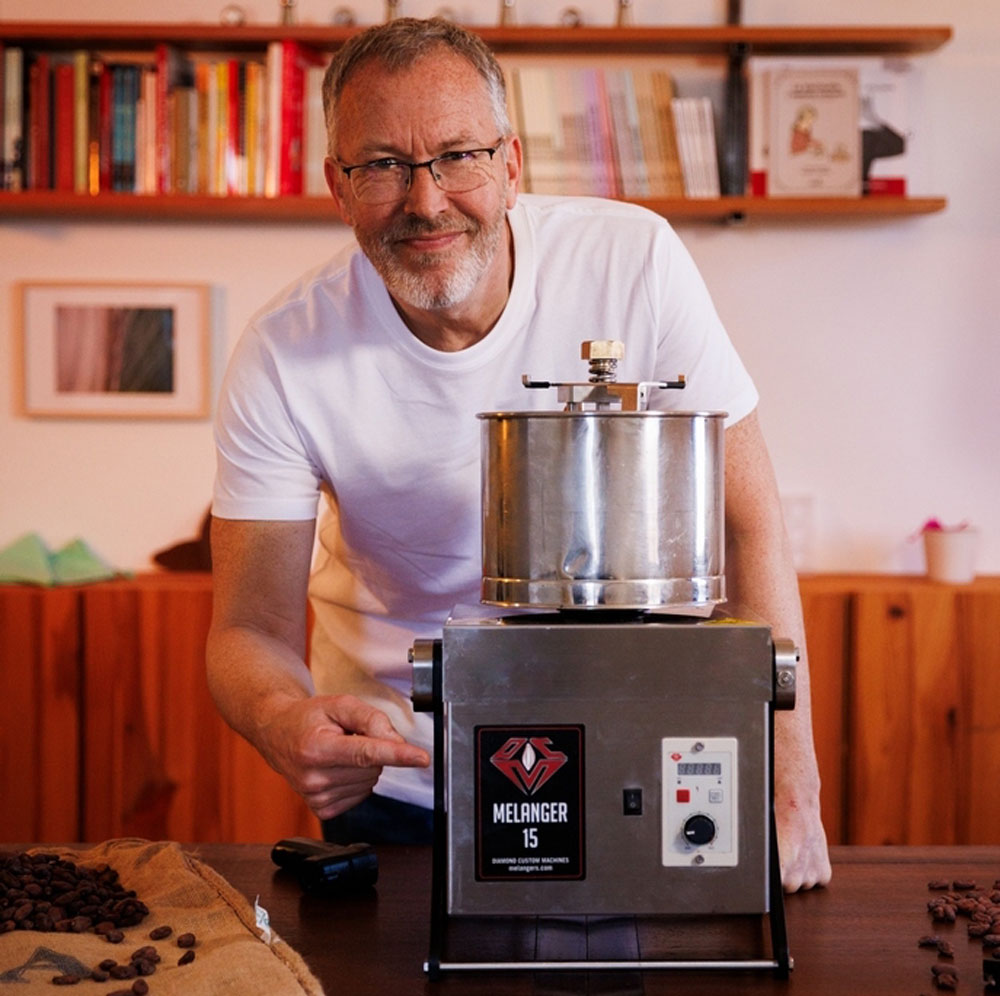 Damian Allsop al costat d'una màquina d'atemperar xocolata professional en un entorn d'elaboració Bean to Bar.